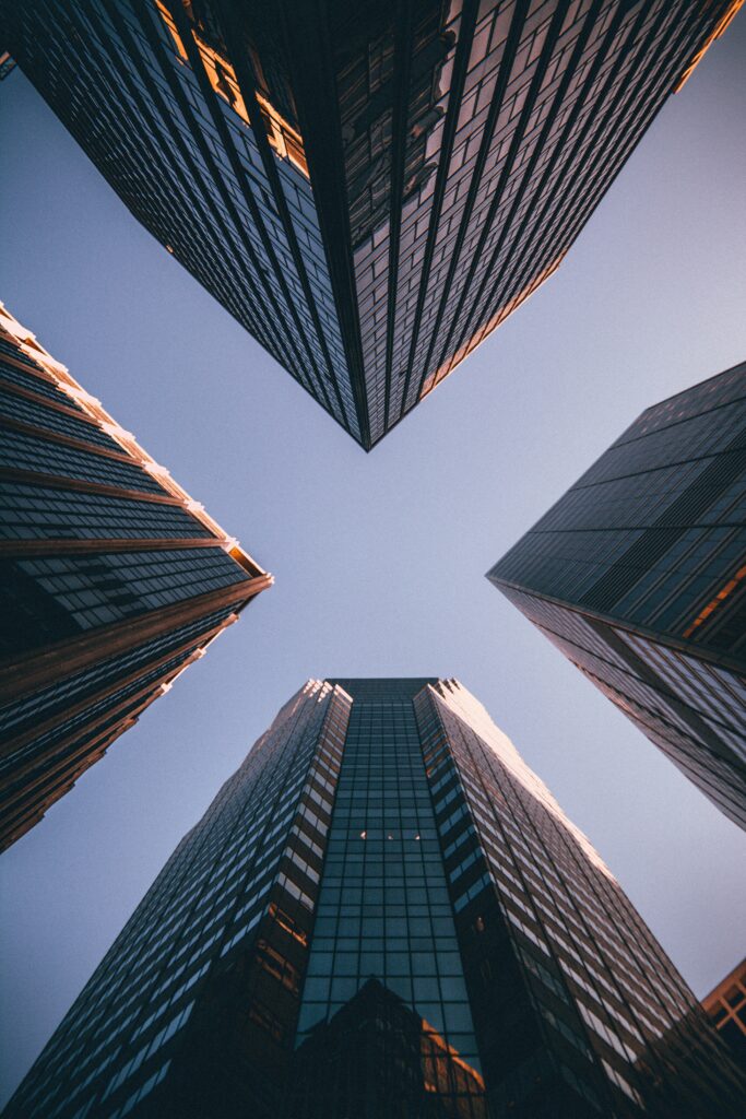 Vue en contre‑plongée de quatre gratte‑ciel modernes en verre sous un ciel bleu, représentant la solidité, la croissance et le dynamisme du milieu des affaires.