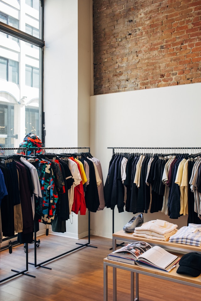 Intérieur d’une boutique de vêtements avec racks, table d’articles pliés et grande fenêtre donnant sur la rue, illustrant le commerce de détail et les besoins de financement pour l’achat d’inventaire massif avant le temps des Fêtes ou le Black Friday.