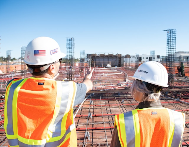 Deux professionnels du bâtiment supervisant un chantier de construction sous un ciel bleu, illustrant le secteur de la construction et de la rénovation et les besoins de financement pour l’achat de matériaux avant le paiement final du client.