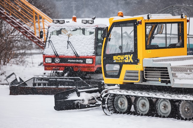 Deux véhicules de déneigement — un jaune et un rouge — stationnés sur un terrain enneigé, représentant les besoins de financement en équipements et opérations hivernales.